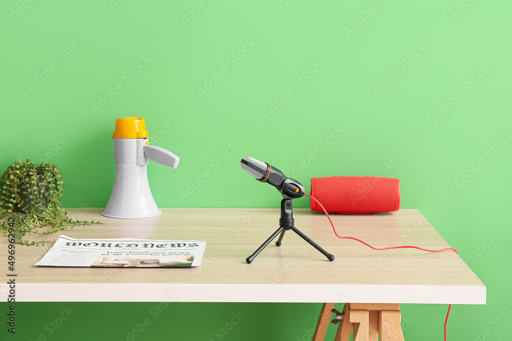 Modern workplace with professional microphone, speaker and megaphone near green wall