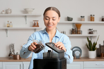 Wall Mural - Young woman putting beans into coffee machine in kitchen