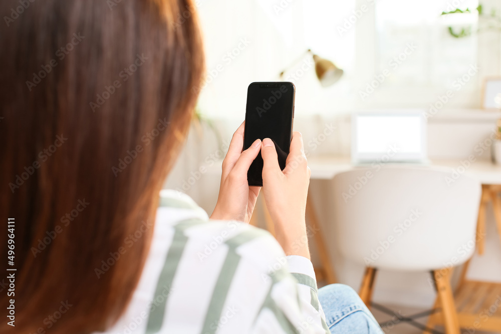 Woman with modern mobile phone reading message in light room