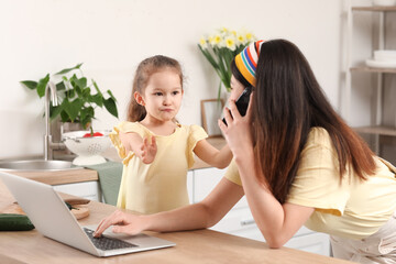 Wall Mural - Little daughter keeping mother from her work at home