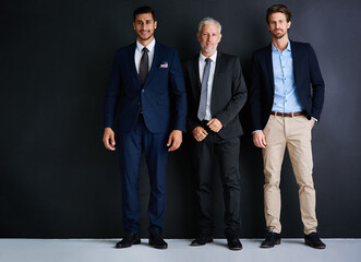 Poster - Three is the magic number for success. Studio portrait of three businessman standing against a black background.