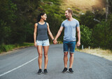 Fototapeta Las - Going the extra mile for love. Shot of a happy young couple walking down a road outside.