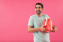 Happy Young Man Holding Gifts In His Hands Against Pink Background