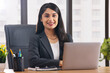 © IndiaPix - Portrait of a happy businesswoman working at desk in office using laptop