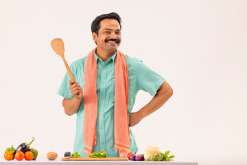 Wall Mural - Cook servant posing in front of camera with holding wooden spatula in kitchen