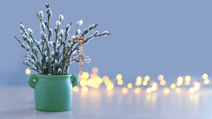 christianity cross rosary and willow branches in vase on table, blurred background. Easter holiday, Orthodox palm Sunday. Symbol of Christianity, Lent, Faith in God, Church holiday. copy space