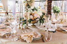 Wedding. Banquet. Decor. Festive Tables On The Terrace In The Forest Are Decorated With Compositions Of White Flowers And Greenery, There Are Candles, Plates With Numbers, Plates And Glasses