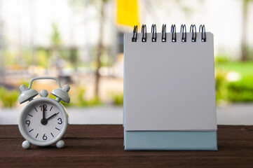 Alarm clock pointing at 2 o'clock with blank notepad on a bench. Copy space concept