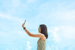 © dodotone - Happy adult asian woman using smartphone take a  selfie photo sky background