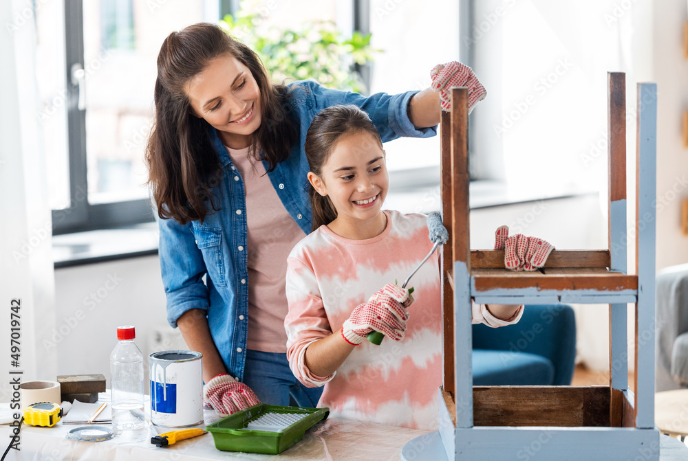 renovation, diy and home improvement concept - mother and daughter in gloves with paint roller painting old wooden table in grey color at home