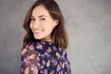 portrait of happy brunette woman smiling and looking beautiful standing isolated on grey concrete ba