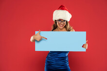 Christmas, X-mas, People, Advertisement, Sale Concept - Happy Woman In Blue Dress And Santa Helper Hat With Blank Blue Board On A Red