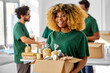 © Syda Productions - charity, donation and volunteering concept - happy smiling female volunteer with food in box and international group of people at distribution or refugee assistance center