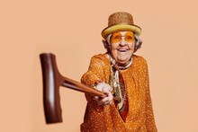 Happy Smiling Stylish Elderly Grandmother Aiming At Camera With A Cane At Studio Over Beige Background. Funny Portrait. Copy Space.