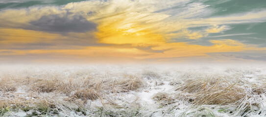 Wall Mural - beautiful dramatic landscape of the transitional season snow-covered field at sunset early spring or late autumn