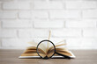 open book with magnifying glass on the table, copy space over white brick wall background