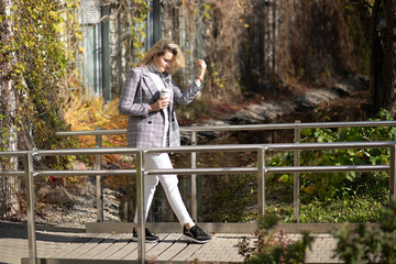 Blond woman relaxing walking wooden bridge with cup coffee, nature outdoor golden autumn fall, hair on face, ivy house