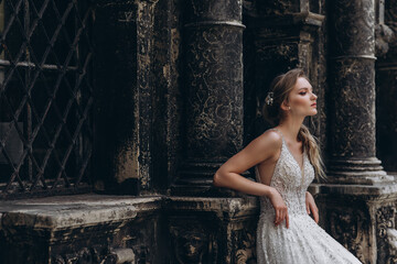 High fashion portrait of young elegant woman outdoor. Bride in white dress near old building.