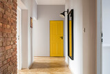 Fototapeta  - Przedpokój z ceglaną ścianą i dużym lustrem oraz żółtymi drzwiami