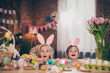 Poster - Portrait of attractive cheerful siblings drawing eggs hiding behind desk desktop table having fun domestic custom indoors