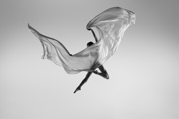 Wall Mural - Black and white portrait of graceful ballerina dancing with fabric, cloth isolated on grey studio background. Grace, art, beauty concept. Weightless, flexible.