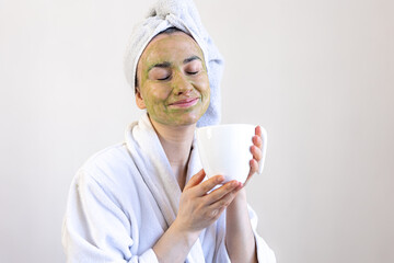 Wall Mural - Young woman with a green beauty mask on her face and with a cup.