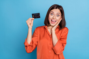 Sticker - Portrait of attractive cheerful amazed girl holding in hand bank card nfc method great news isolated over bright blue color background