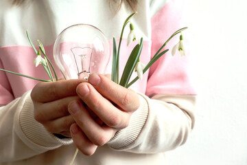 World Environment Day: a light bulb and a bouquet of snowdrops in the hands of a child, close-up, space for text