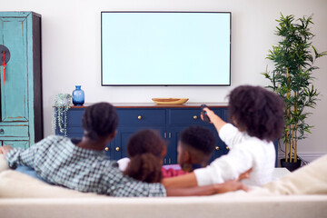 Wall Mural - Rear View Of Family Sitting On Sofa Watching Movie On TV At Home