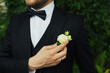 Close-up of the groom's boutonniere from white roses, bow, white shirt and black jacket. Bearded groom adjusting the boutonniere