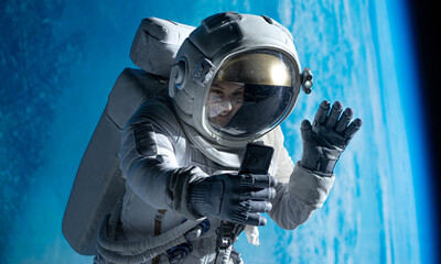 Wall Mural - female astronaut having a video call on her phone while performing spacewalk in open space, earth in