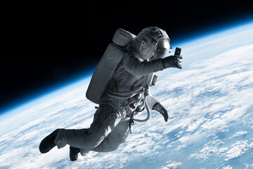 female astronaut having a video call on her phone while performing spacewalk in open space, earth in