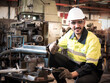 © panyajampatong - Confident Middle Eastern technician worker wearing a safety helmet and vest standing on the machine and thumb up and smile in the industrial factory.