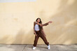 Woman dancing in front of beige wall wide stance with arms to side