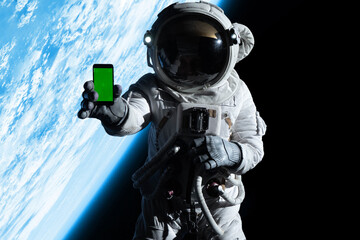 Wall Mural - astronaut showing a screen of a phone into a camera while performing spacewalk in open space, earth 