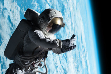 Wall Mural - female astronaut having a video call on her phone while performing spacewalk in open space, earth in