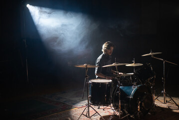 Young drummer sitting in spotlight and training in hall. Concentrated rock musician rehearsing or recording drums. Drummer training concept