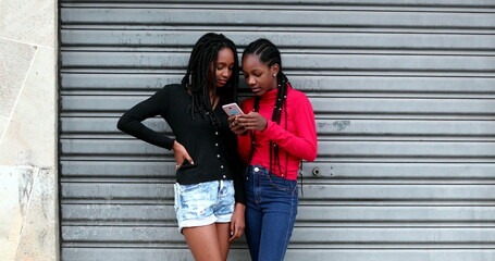 Canvas Print - Candid black teens girls using cellphone, adolescent girl in shock gossiping with friend