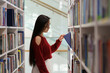© DimaBerlin - Asian student girl standing between library bookcases, young korean woman picking up book from shelf while studying in university library, using learning materials. Educational opportunities
