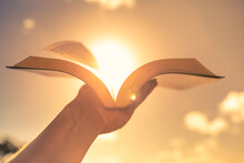 Hand Holding Open Book Bible Up To The Sunlight