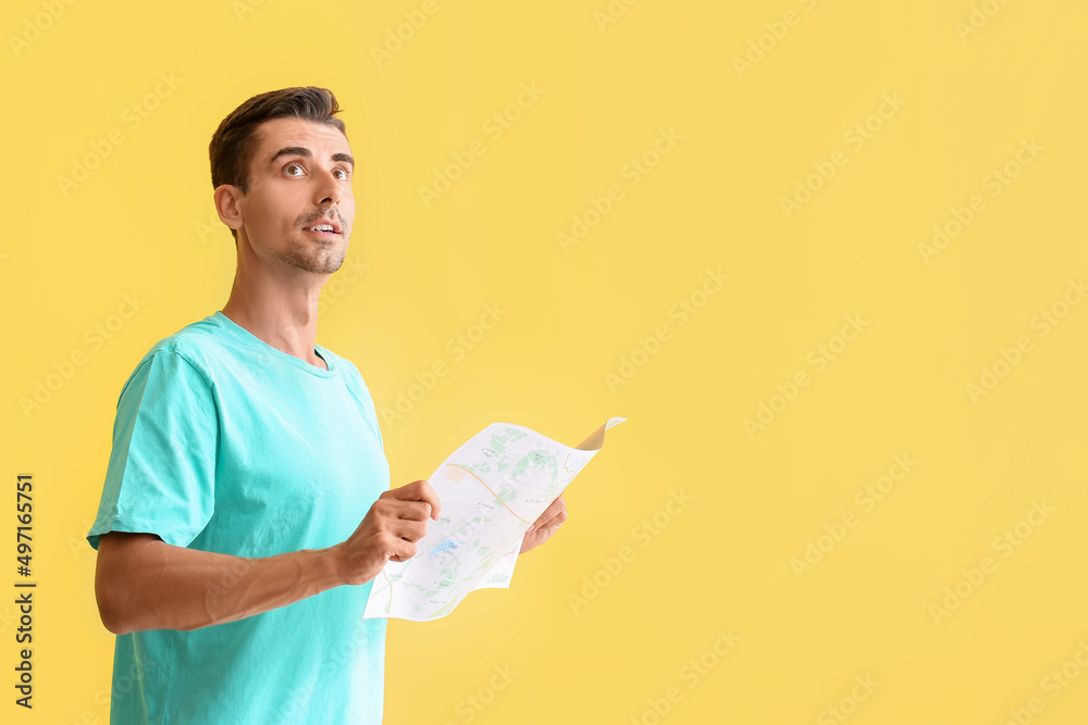 Young male tourist with map on color background