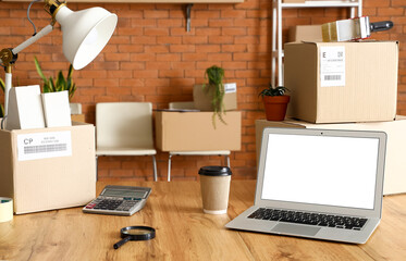 Wall Mural - Cardboard boxes with belongings and laptop on table in office on moving day