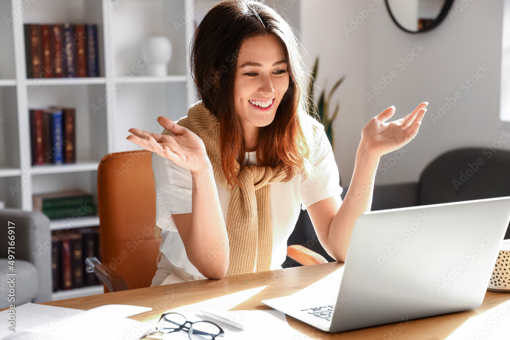 Young Asian tutor with laptop giving lesson online at home