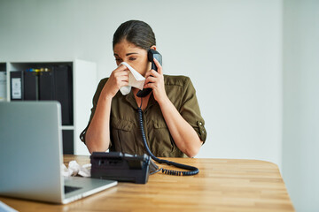 Poster - its an unbearable condition to work in. shot of a young businesswoman blowing her nose while speakin