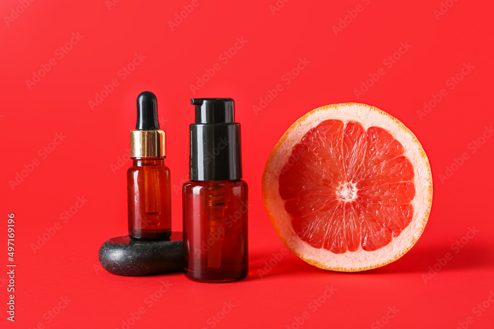 Bottles with essential oil and half of grapefruit on red background