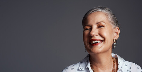 Keep the good times rolling. Studio shot of a senior woman sitting on a chair against a grey background.