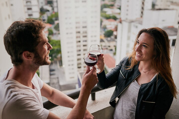 Wall Mural - Celebrating our adventure through the city. Cropped shot of an attractive young couple drinking wine on a rooftop looking over the city.