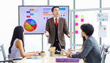 Fototapeta  - Asian professional successful businessman manager standing showing company growth profit target graph chart presentation on computer monitor to young male and female colleagues in office meeting room