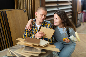 Wall Mural - Young smiling couple choosing laminated material for home in building hypermarket