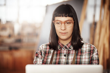 Poster - Focused on achieving her design goals. Cropped shot of an attractive young woman working on her laptop while sitting in her creative workshop.